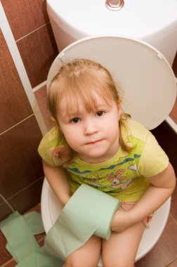The little girl sits on a toilet bowl