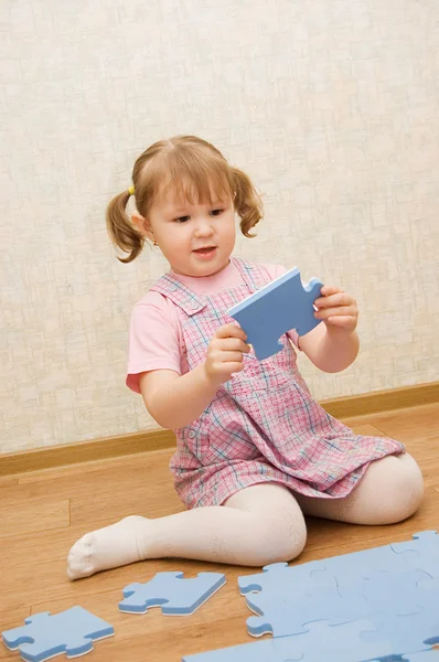 Little girl collects puzzles in a room — Stock Photo, Image