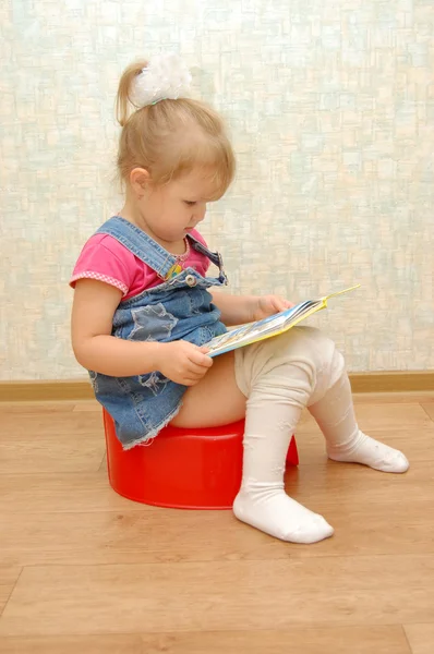Niña sentada en el orinal rojo con libro abierto — Foto de Stock