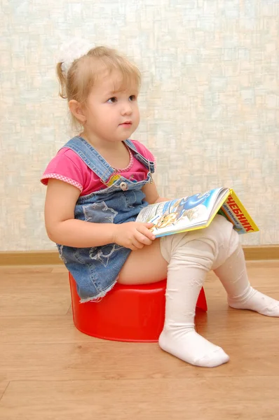 Menina sentada no penico vermelho com livro aberto — Fotografia de Stock
