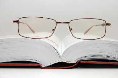 Spectacles laying on the open book clipart