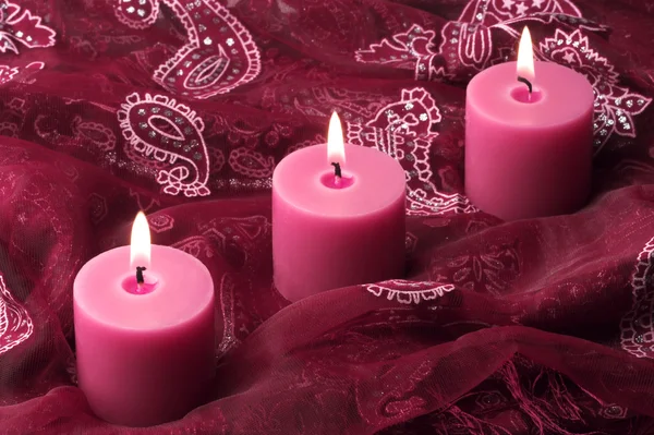 Три свечи на фиолетовой ткани — стоковое фото