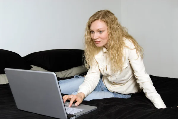 女子躺在她床上用的笔记本电脑. — 图库照片