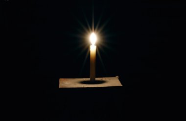 Burning candle on a black background clipart