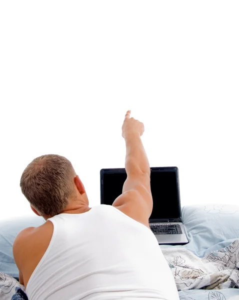 Young man indicating with laptop on bed — Stock Photo, Image