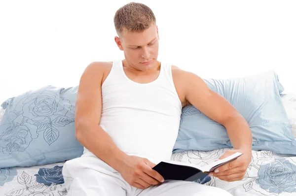 Knappe mannelijke leesboek in bed — Stockfoto