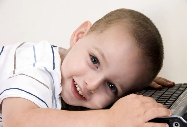 Kleine jongen liggend op laptop, glimlachend — Stockfoto