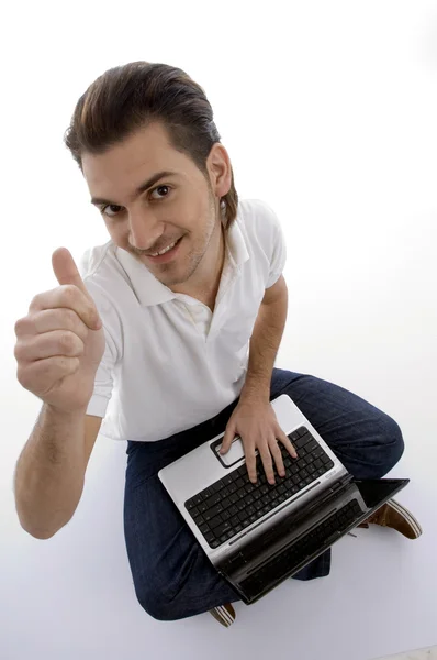 Mladý muž sedí s notebookem, palec nahoru — Stock fotografie