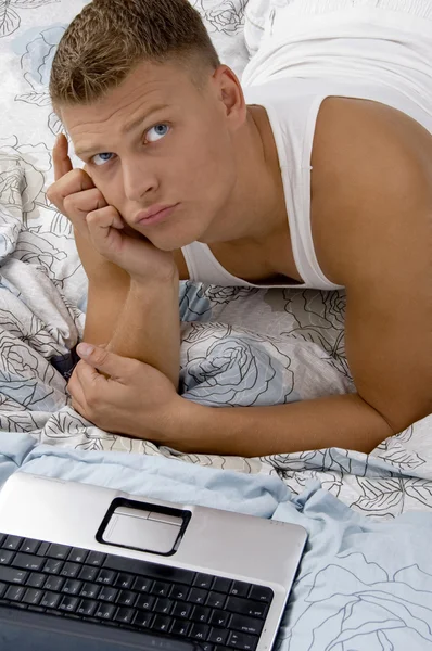 Νεαρός άντρας σκέφτεται με laptop στο κρεβάτι — Φωτογραφία Αρχείου