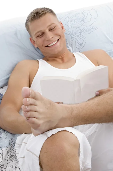 年轻小伙子读本书躺在床上 — 图库照片