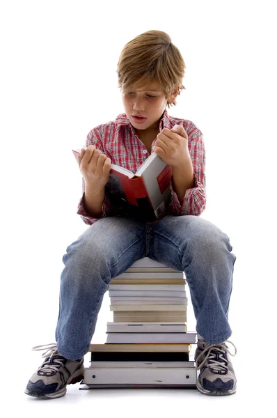 Boy sitting on pile of books and reading — Stock Photo, Image