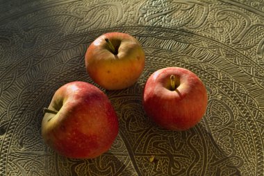 Three red organic apples on an arabic beaten out metal table. clipart