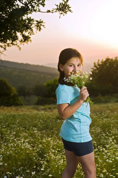 Flicka med blommor i fältet vid solnedgången — Stockfoto