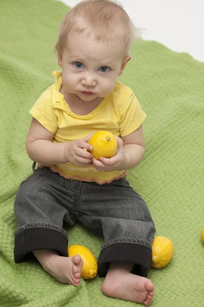 Baby eten een citroen op groene achtergrond — Stockfoto