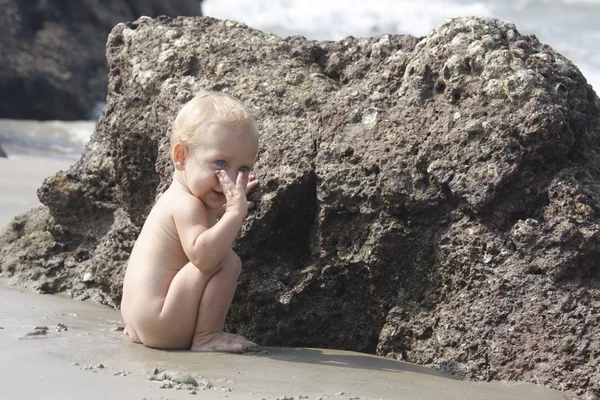 Младенец играет на пляже у камня — стоковое фото
