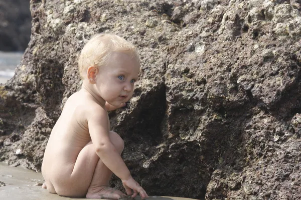 Baby playing on the beach near the stone — Stok fotoğraf