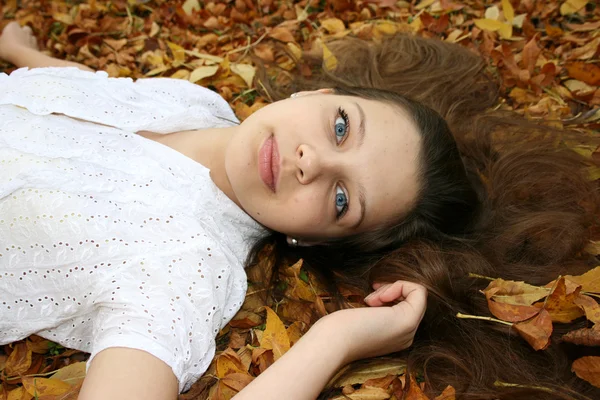 Девушка с голубыми глазами, лежащими в листьях — стоковое фото
