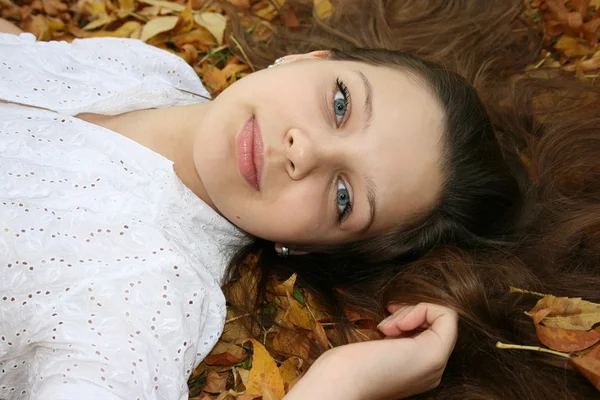 Mädchen mit blauen Augen in den Blättern liegend — Stockfoto