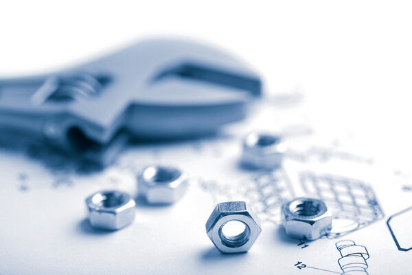 Гаечный ключ и гайки поверх технического чертежа
