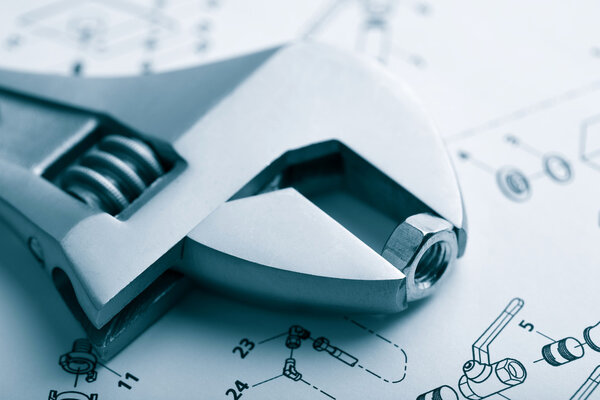 Гаечный ключ и гайка поверх технического чертежа
