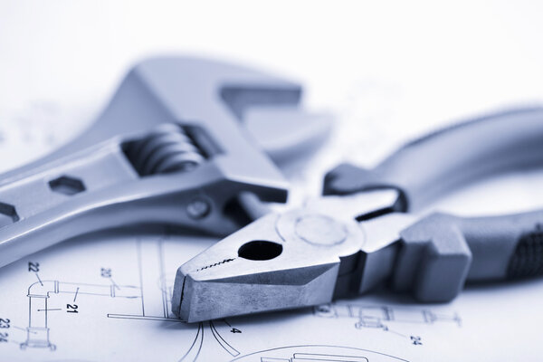 Гаечный ключ и плоскогубцы поверх технического чертежа

