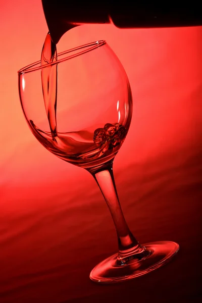 Wine pouring into glass over red — Stock Photo, Image