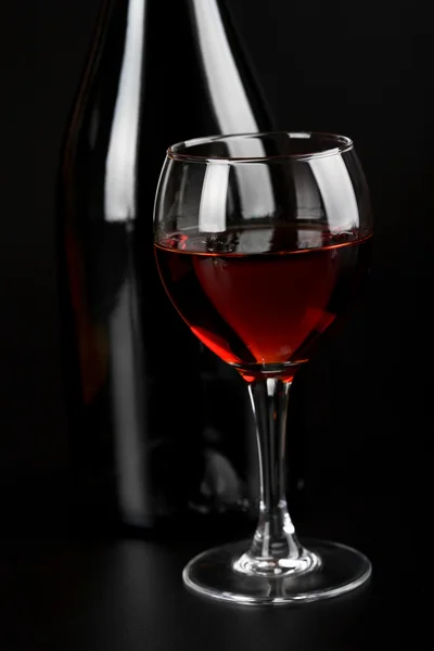 Glass of red wine and bottle over black — Stock Photo, Image