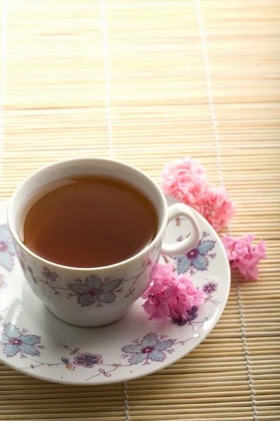 Tazza di tè e fiori sopra il tappetino di bambù — Foto Stock