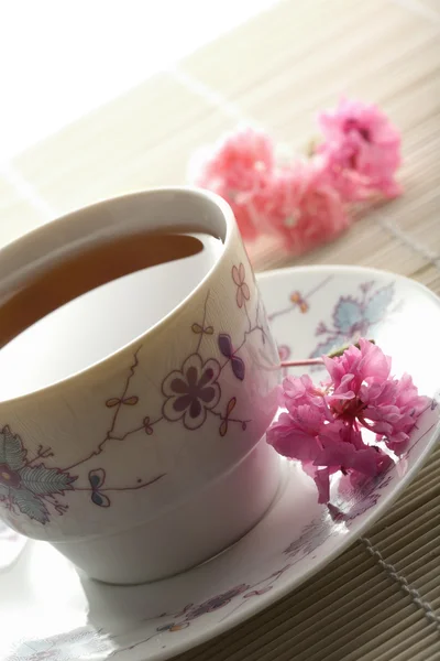 Cup of tea and flowers over bamboo mat — Stock Photo, Image