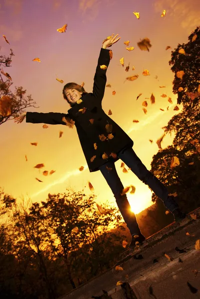 年轻女孩投掷秋季叶片在日落时间 — 图库照片