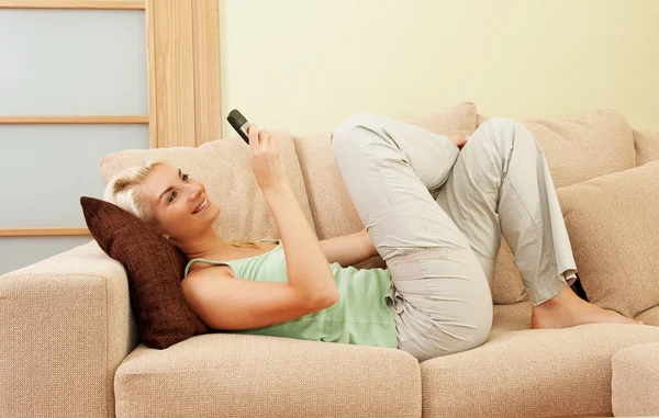 Mulher deitada em um sofá e escrevendo sms — Fotografia de Stock