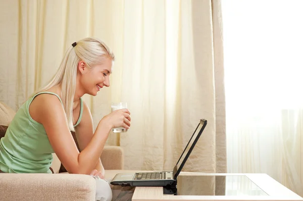 Женщина пьет молоко и использует ноутбук — стоковое фото