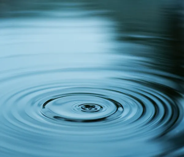 Droplet faller i blått vatten — Stockfoto