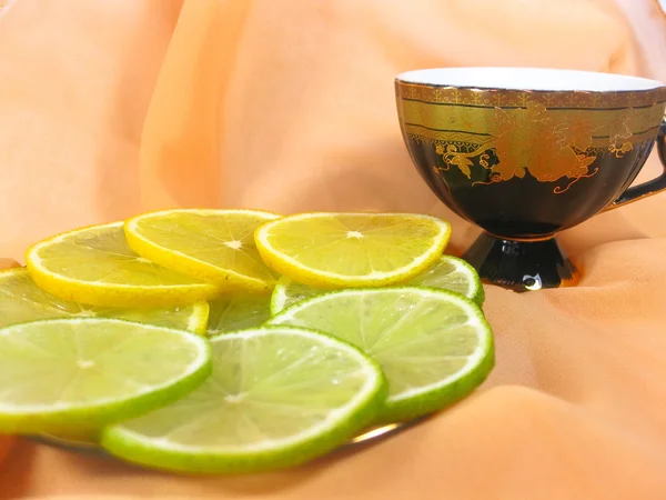 Limón y lima con una taza de té y una p — Foto de Stock