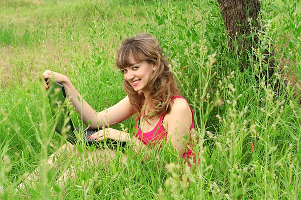 Sonriente chica joven con ordenador portátil en la hierba — Foto de Stock