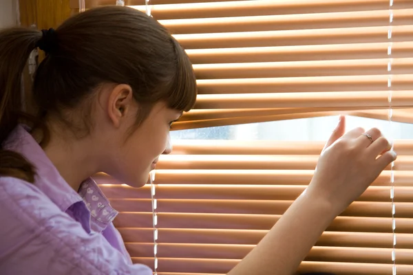 Adolescente menina olha pela janela — Fotografia de Stock