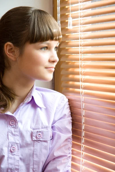 Menina bonita olha pela janela — Fotografia de Stock