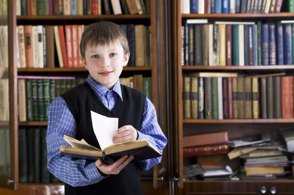 Αγόρι στη βιβλιοθήκη που κατέχουν το βιβλίο — Φωτογραφία Αρχείου