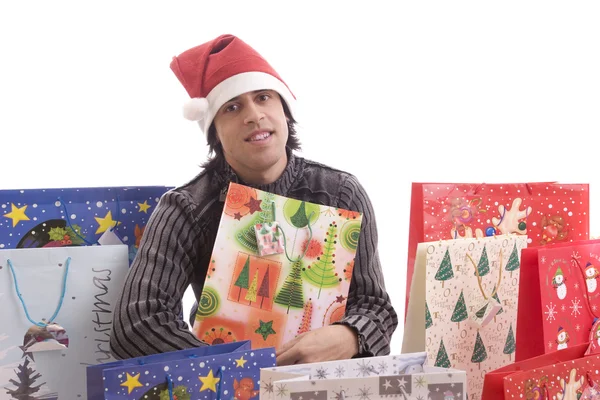Junger Mann mit Weihnachtsmütze, voller Geschenke — Stockfoto