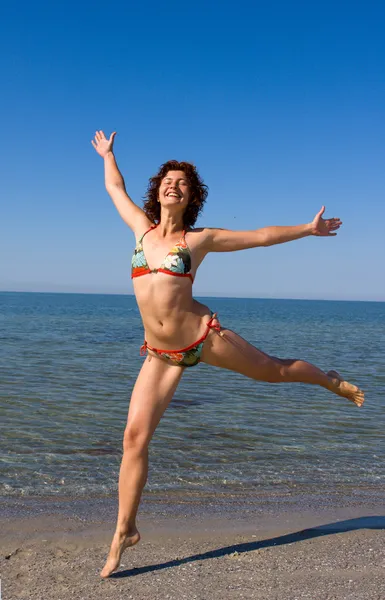 Menina sorridente feliz pulando na praia do mar — Fotografia de Stock