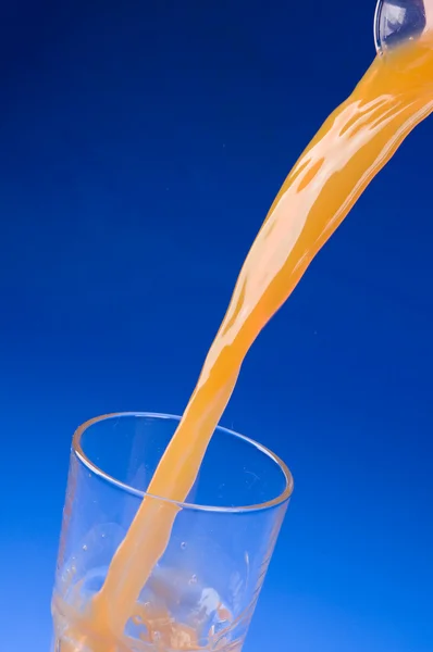 Despejando suco de laranja fresco sobre azul — Fotografia de Stock