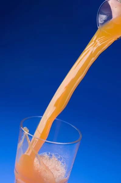 Pouring fresh orange juice over blue — Stock Photo, Image