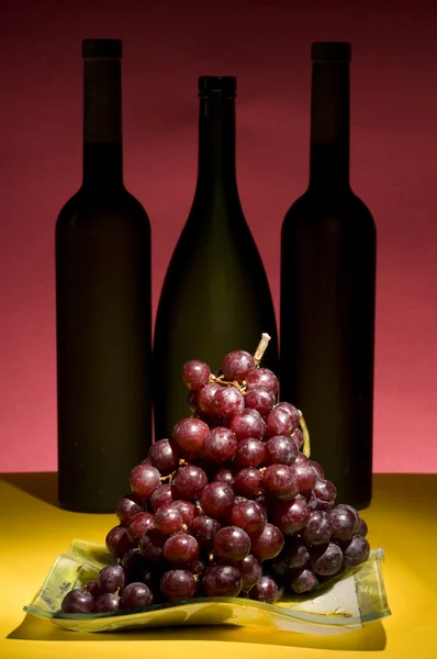 Röda druvor och vin flaska stilleben — Stockfoto