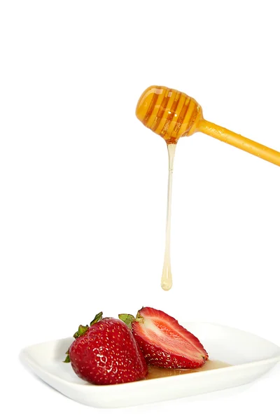 Honey dripping from a stick to strawberries — Stock Photo, Image
