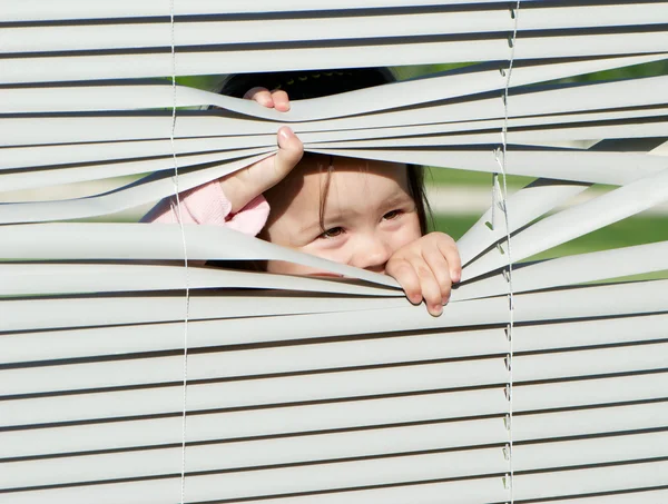 Meisje kijkend door de blinds — Stockfoto