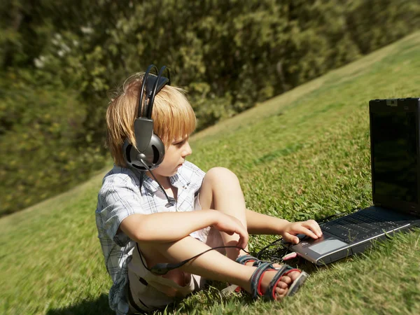 Мальчик с ноутбуком и наушниками в па — стоковое фото