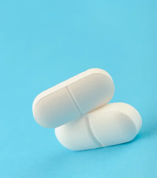 Dos comprimidos blancos sobre fondo azul . — Foto de Stock