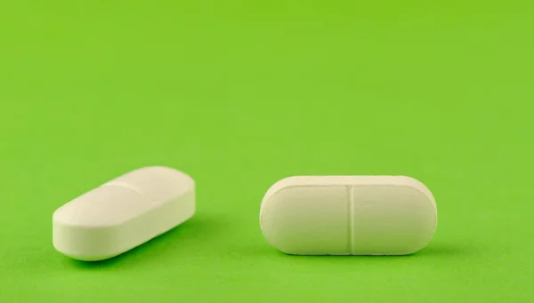 Twee witte tablet op een groene achtergrond. — Stockfoto