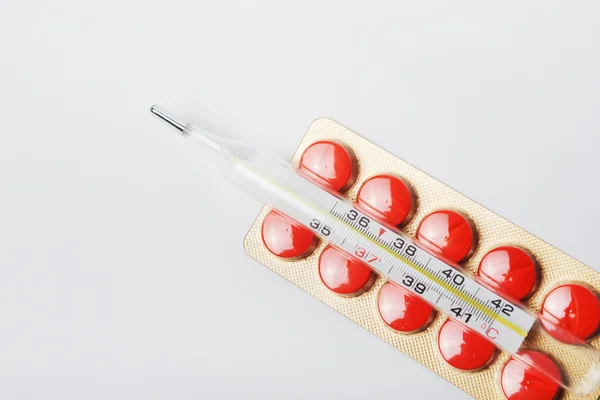 Termômetro em um pacote de comprimidos vermelhos — Fotografia de Stock