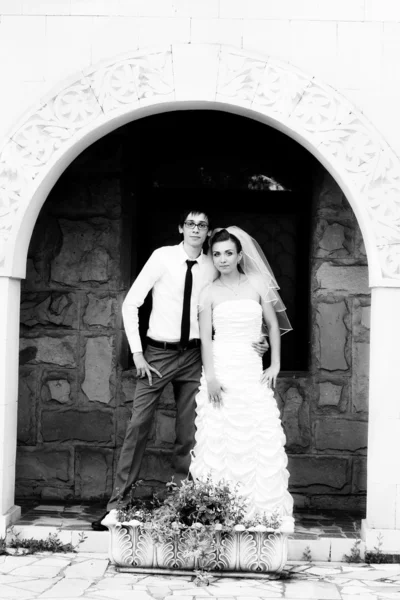 Recién casados se levanta contra una pared de ladrillo en el arco —  Fotos de Stock